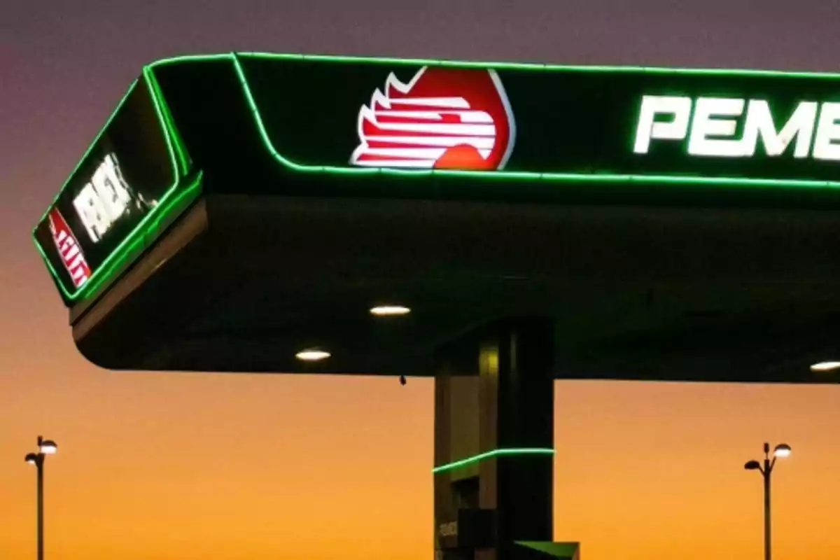 Techo de una estación de servicio con logotipo iluminado al atardecer.