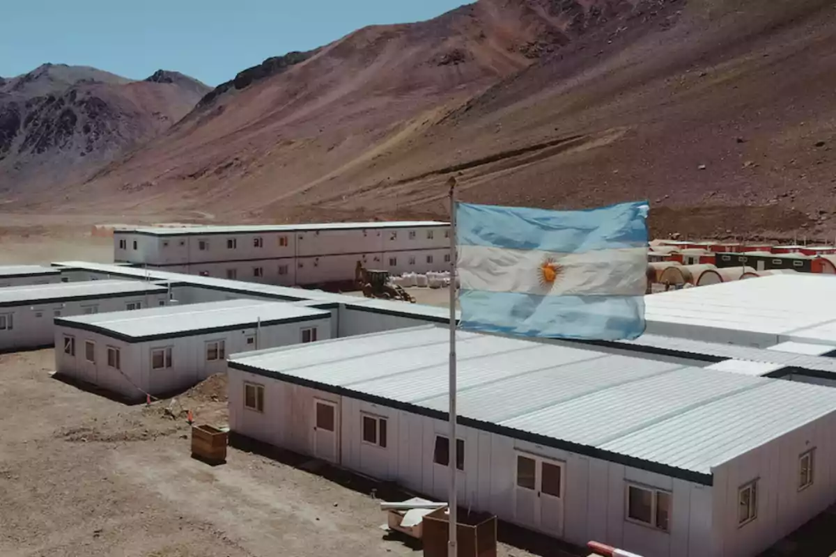 Edificios modulares en un paisaje montañoso con una bandera de Argentina ondeando en primer plano.