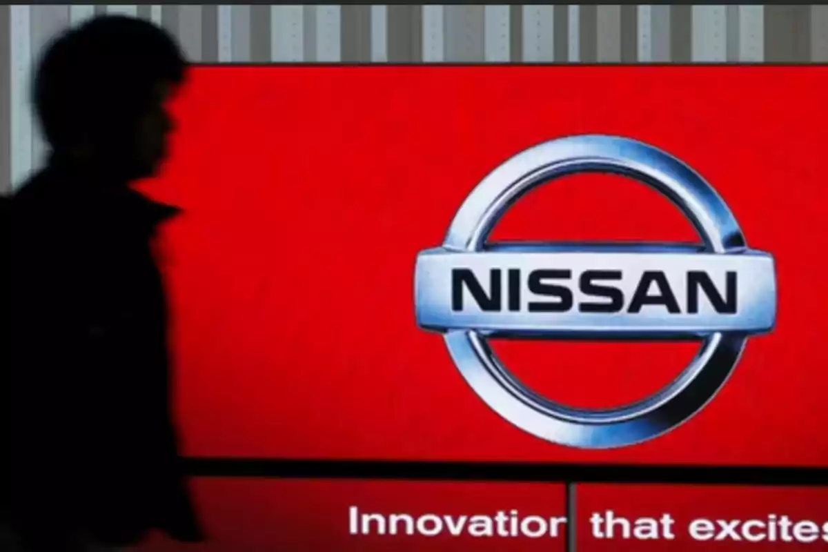 Una persona en silueta pasa frente a un cartel rojo con el logotipo de Nissan y el lema 