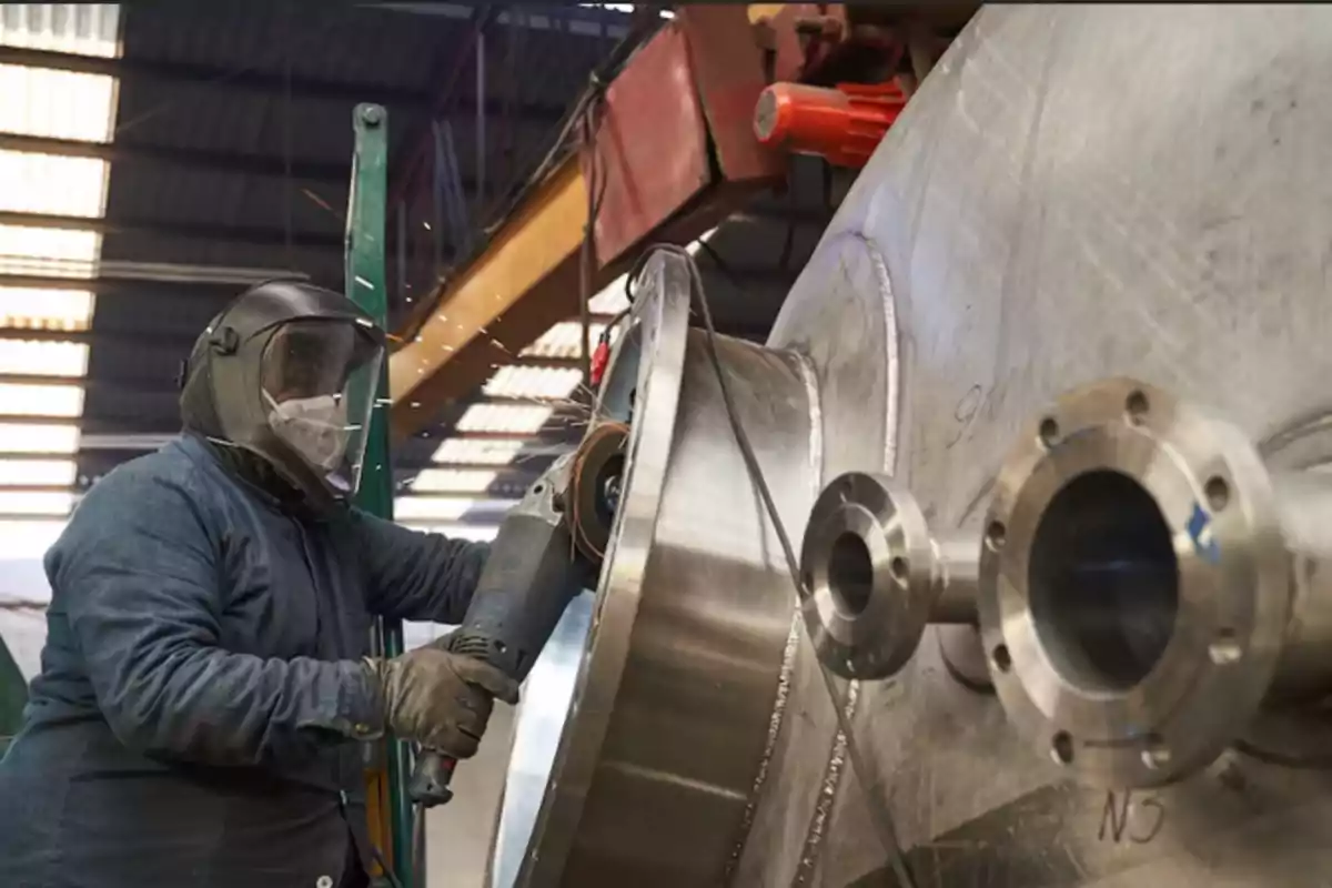 Trabajador con equipo de protección usando una herramienta eléctrica para trabajar en una gran estructura metálica en un taller industrial.