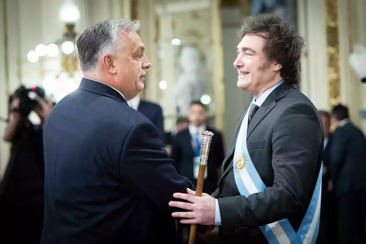 Dos hombres de traje se saludan cordialmente en un entorno elegante y formal.