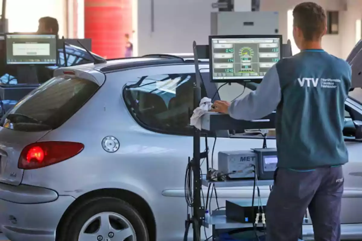 A technician performs a vehicle inspection at a technical verification center, using diagnostic equipment connected to a silver car.