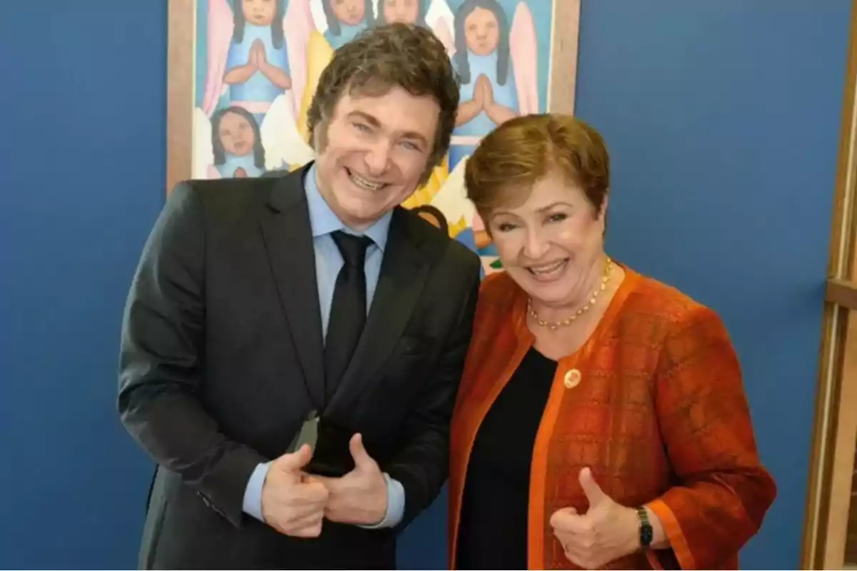 Dos personas sonrientes posan juntas haciendo el gesto de pulgar hacia arriba frente a una pintura colorida.