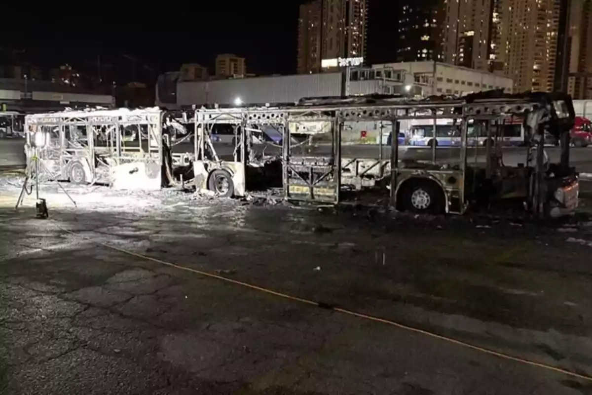 Un autobús completamente quemado en un estacionamiento urbano durante la noche.