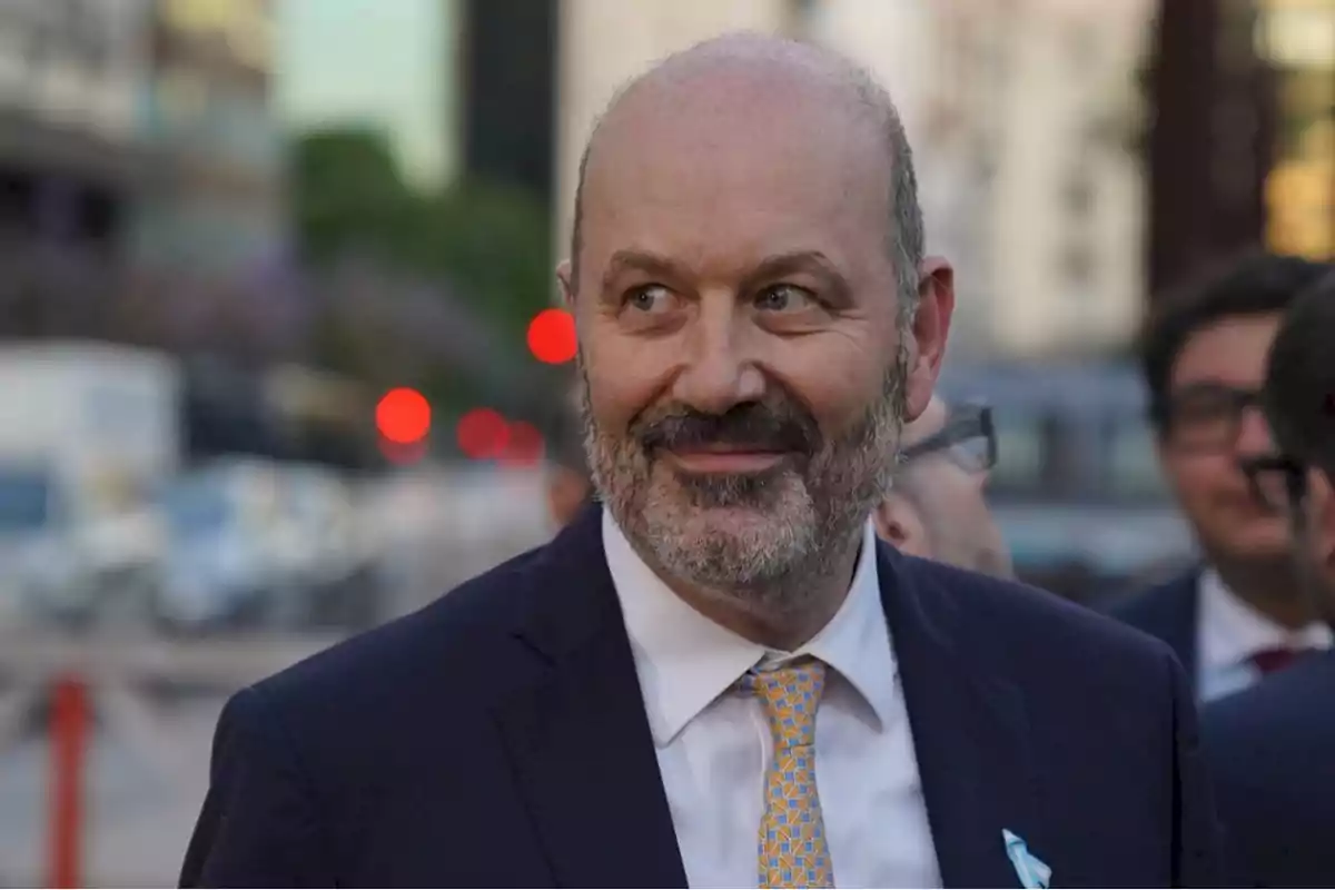 Un hombre con barba y traje sonríe mientras está al aire libre en un entorno urbano.