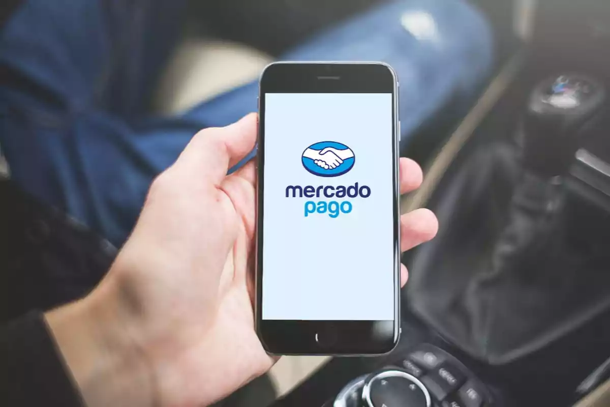 Persona sosteniendo un teléfono móvil que muestra el logo de Mercado Pago en la pantalla dentro de un automóvil.