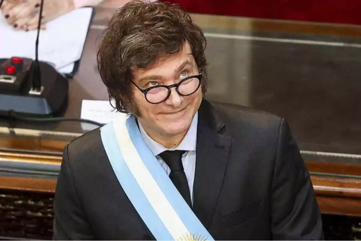 Un hombre con gafas y una banda presidencial en un entorno formal.