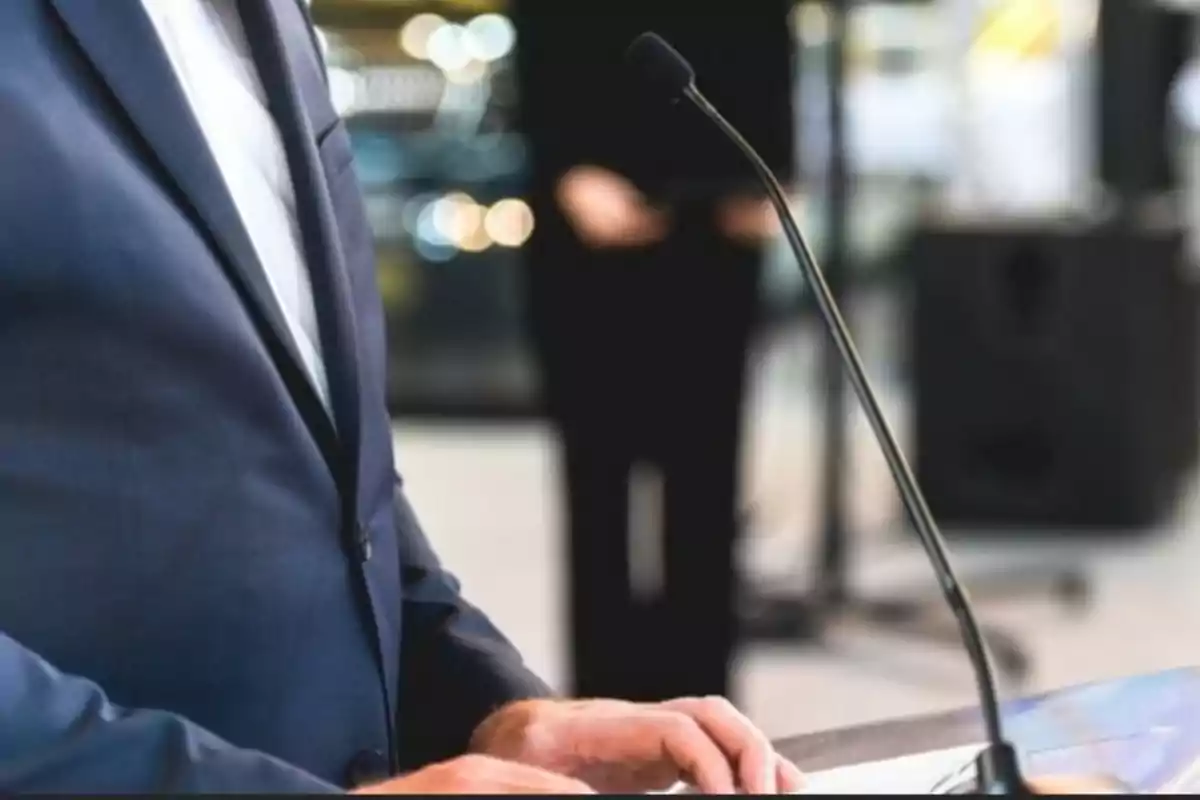 Persona en traje hablando en un podio con un micrófono.