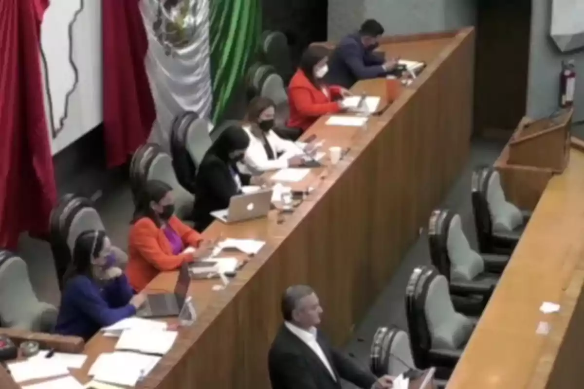 Personas sentadas en un salón de conferencias con banderas en el fondo.