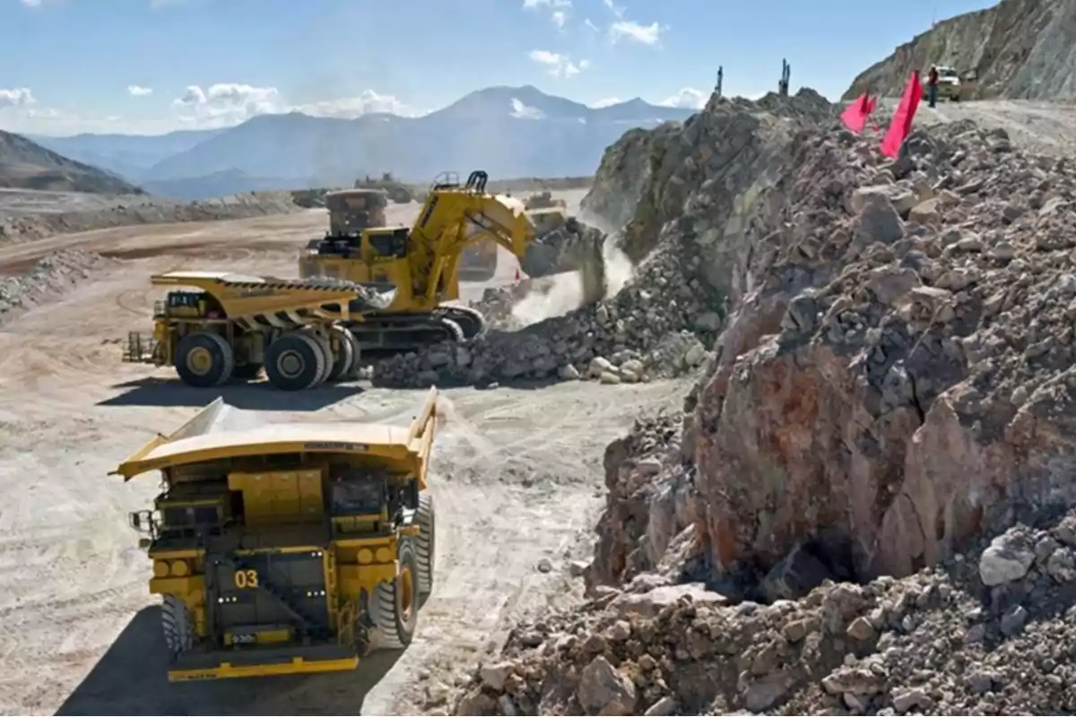 Maquinaria pesada trabajando en una mina a cielo abierto con montañas al fondo.