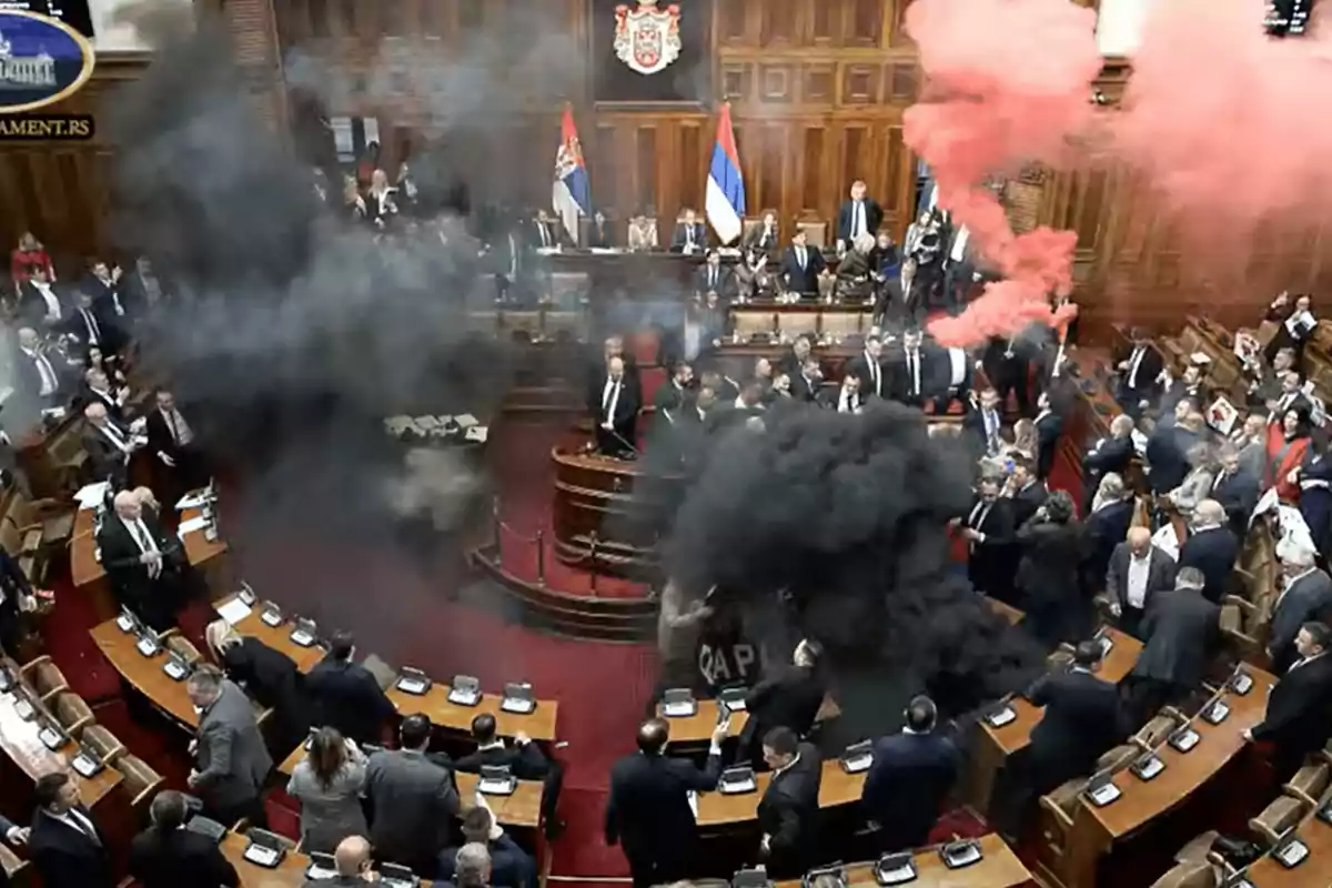 Una escena en un parlamento con humo negro y rojo llenando el recinto mientras los parlamentarios están de pie y observan.