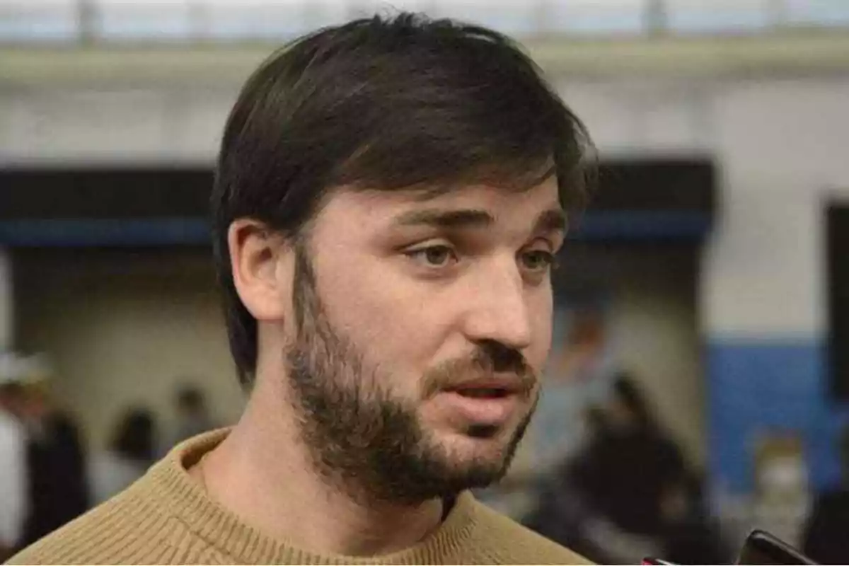 Man with a beard and dark hair speaking in an indoor setting.