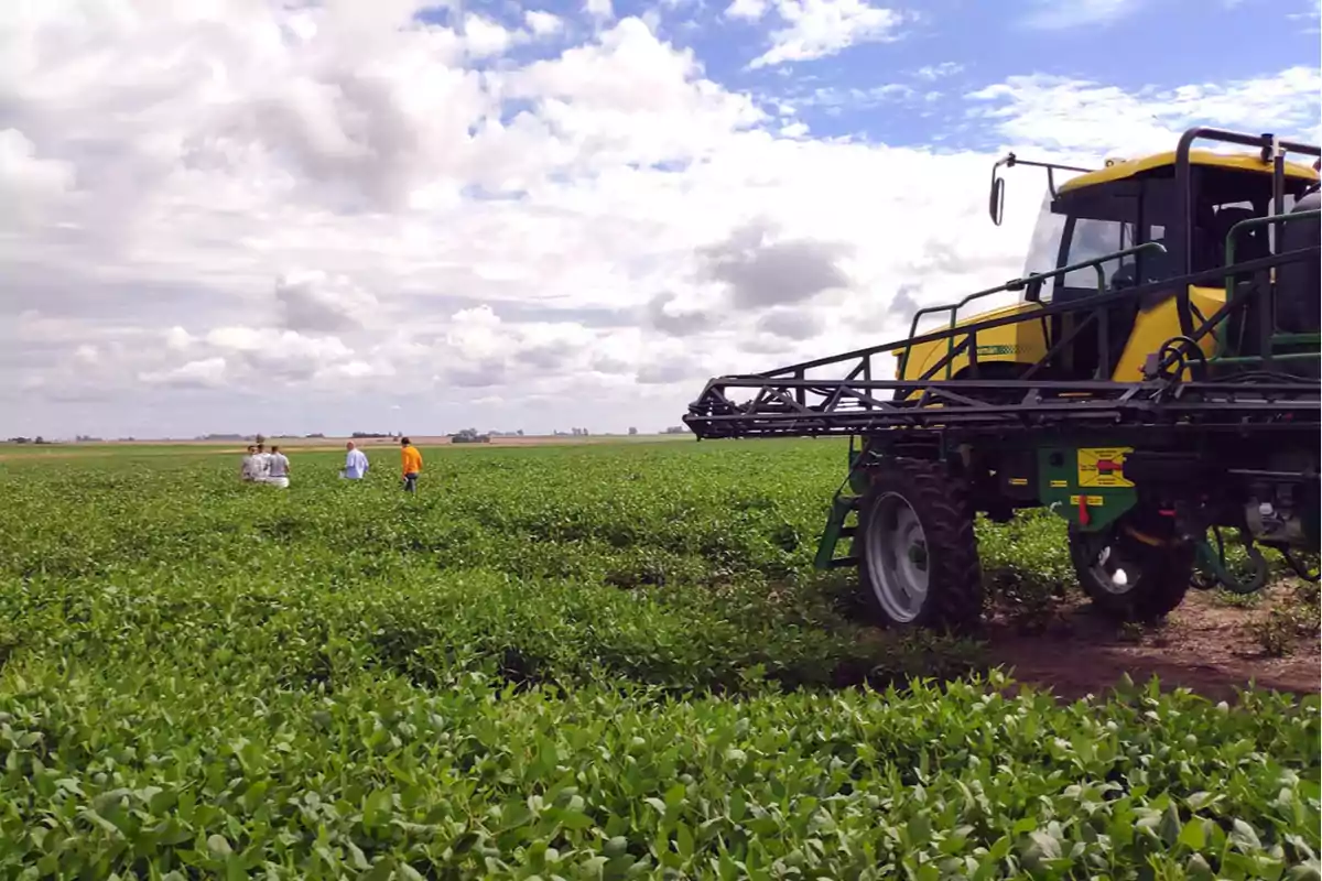 A farmland with a tractor and several people walking among the plants under a partly cloudy sky.