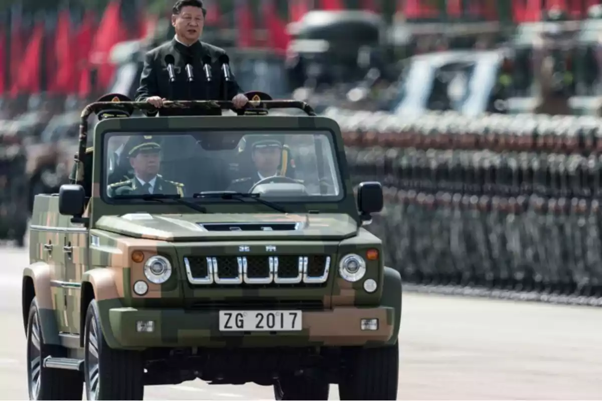 A military leader standing on a camouflaged vehicle during a parade with soldiers lined up in the background.