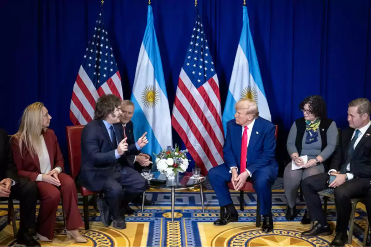 A group of people sitting on chairs at a formal meeting with United States and Argentina flags in the background.