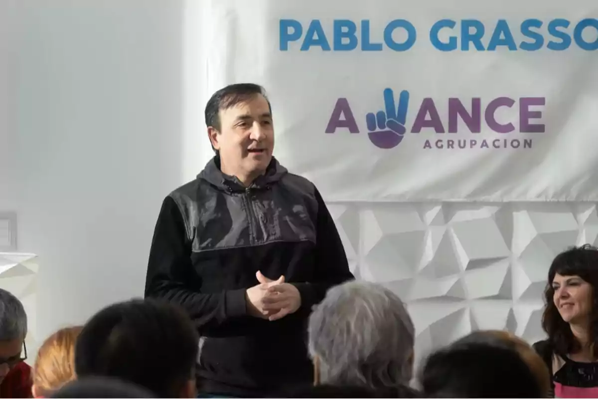 Un hombre hablando frente a un grupo de personas con un cartel de fondo que dice 