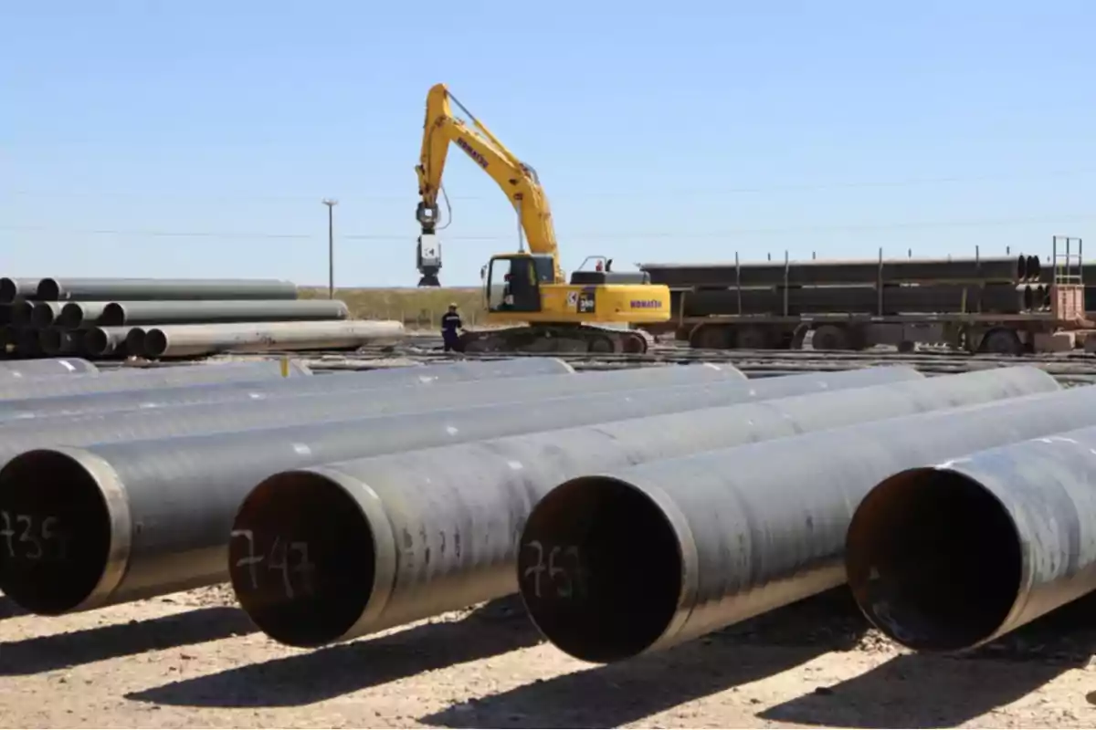 Una excavadora amarilla moviendo grandes tubos de metal en un sitio de construcción al aire libre.