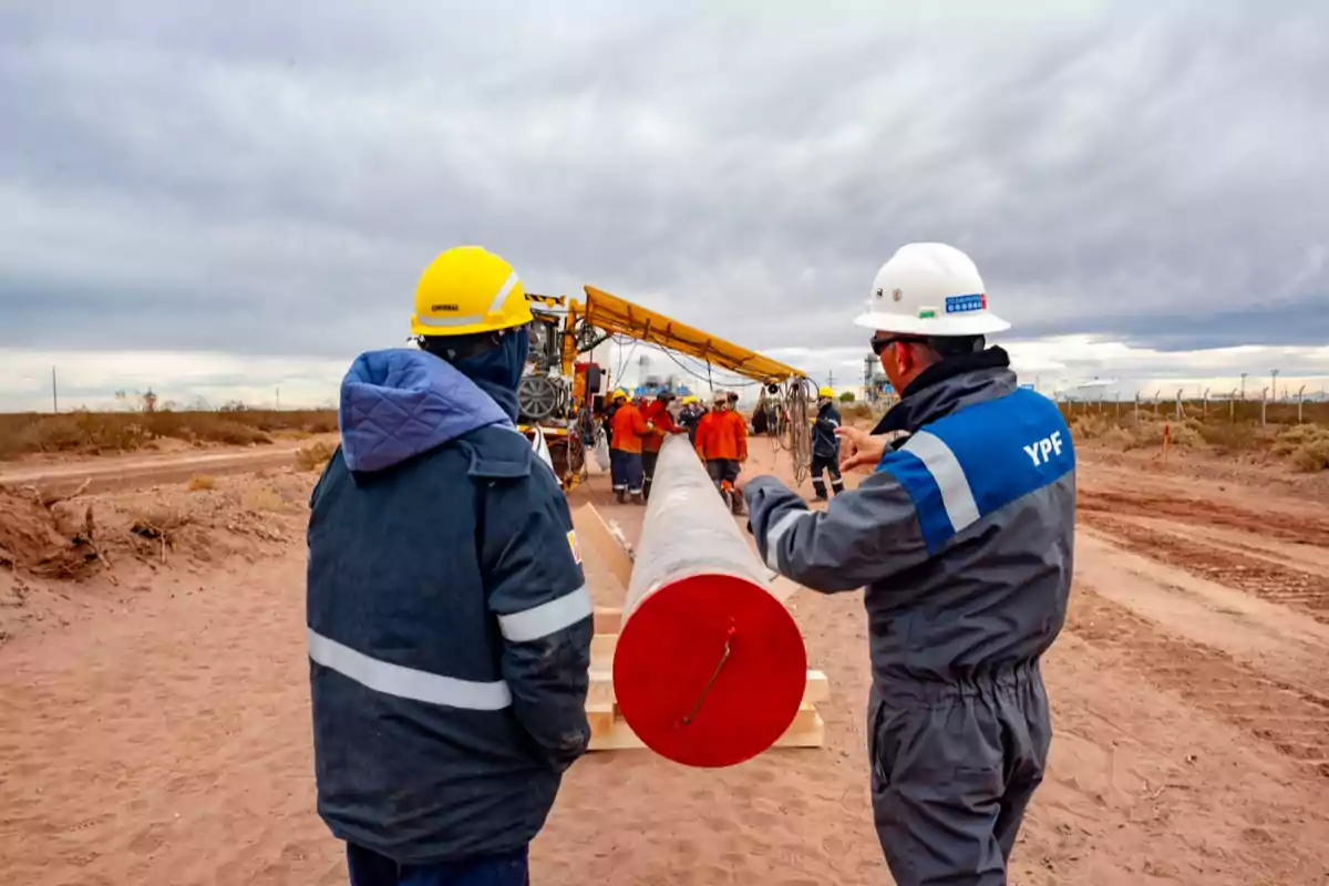 Trabajadores de la construcción inspeccionan un gran tubo en un sitio de obra al aire libre.