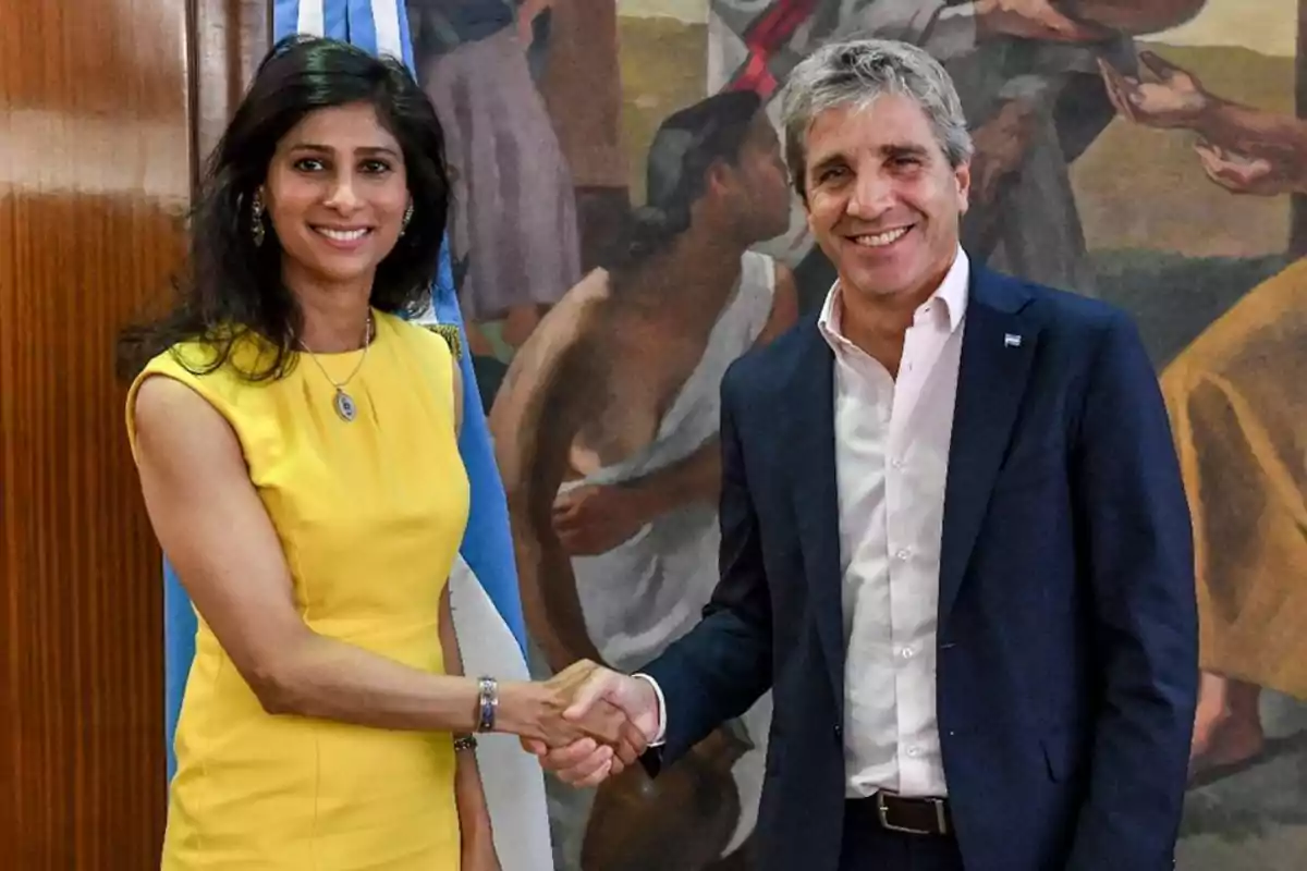 Dos personas dándose la mano frente a una bandera y un mural.