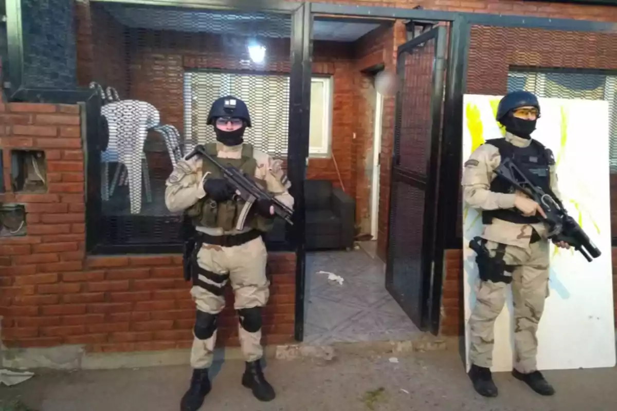 Dos agentes de seguridad armados con equipo táctico frente a un edificio de ladrillo.