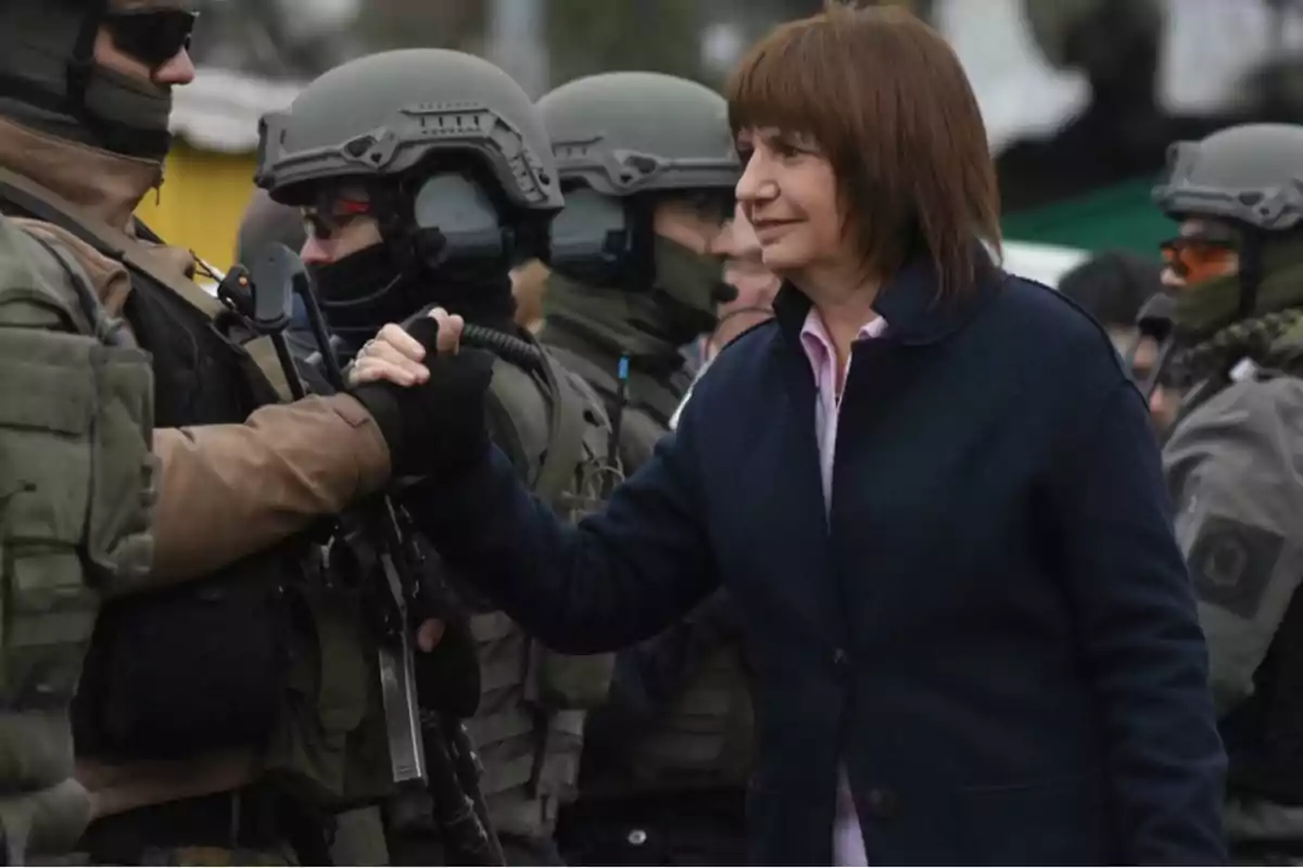 Una mujer estrecha la mano de un miembro de las fuerzas de seguridad que lleva uniforme y casco, mientras otros agentes están en el fondo.