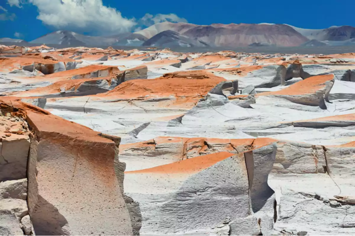 White and orange rock formations in a desert landscape with mountains in the background under a blue sky.