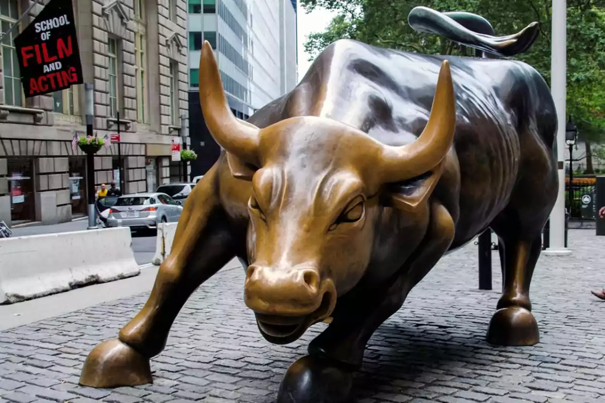 Bronze bull sculpture on a street surrounded by buildings and trees.