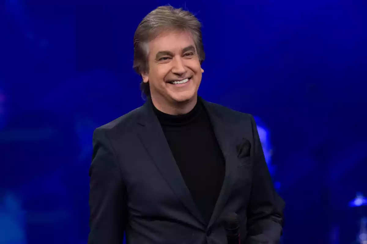 A smiling man in a dark suit with a blue background.