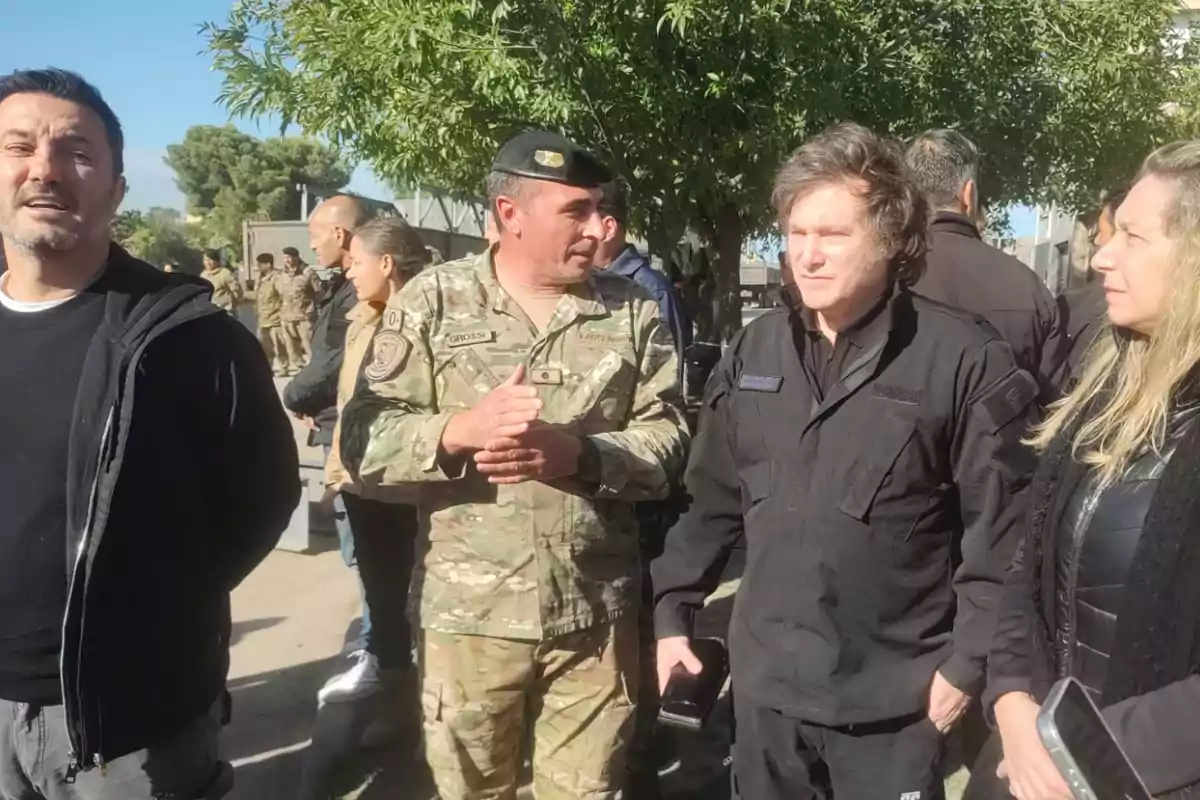 Un grupo de personas, algunas con uniforme militar, conversan al aire libre bajo un árbol.