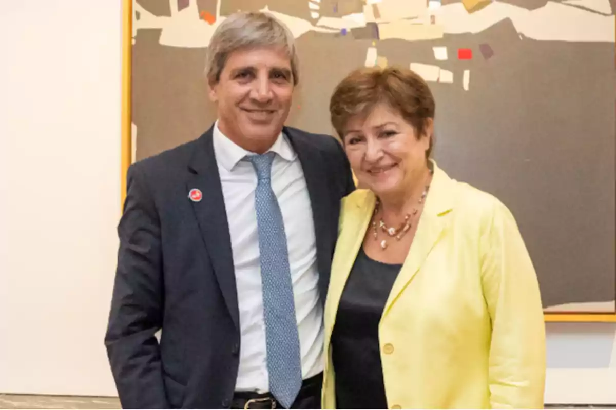 Dos personas posando juntas frente a una pintura abstracta en un entorno formal.