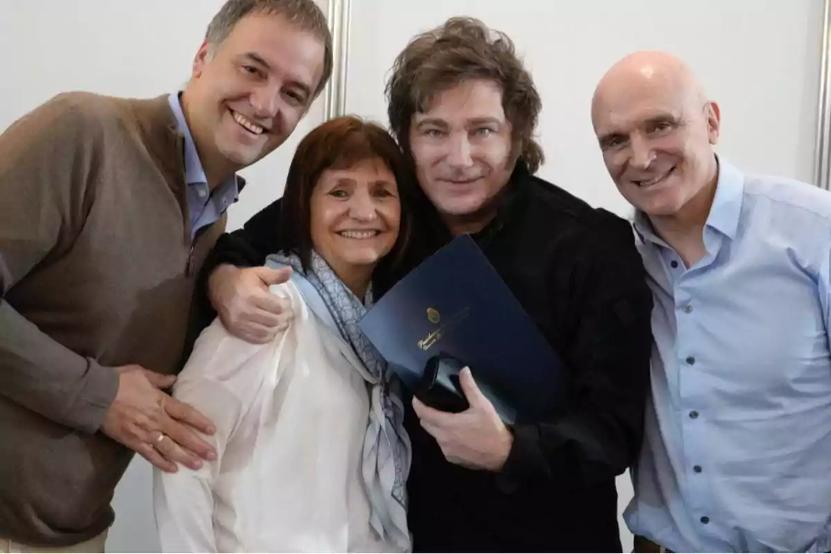 Un grupo de cuatro personas sonríe mientras posan juntas, una de ellas sostiene una carpeta azul.