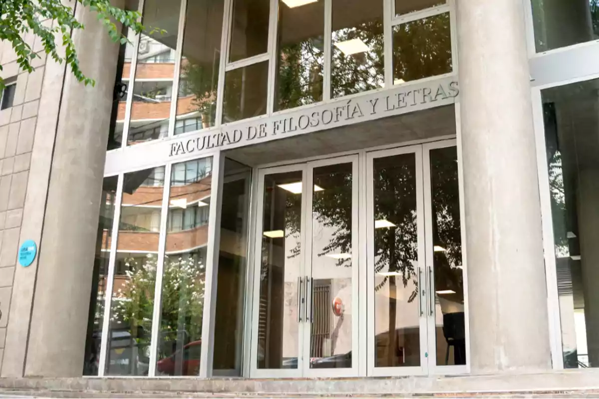 Entrada de un edificio con el letrero "Facultad de Filosofía y Letras" sobre las puertas de vidrio.