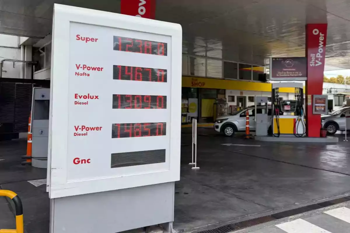 Una estación de servicio con un cartel que muestra los precios de diferentes tipos de combustible, incluyendo Super, V-Power Nafta, Evolux Diesel y V-Power Diesel, con un vehículo estacionado cerca de las bombas de gasolina. Una estación de servicio con un cartel que muestra los precios de diferentes tipos de combustible, incluyendo Super, V-Power Nafta, Evolux Diesel y V-Power Diesel, con un vehículo estacionado cerca de las bombas de gasolina.