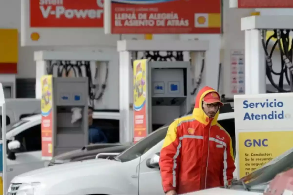 Un empleado de una estación de servicio Shell con uniforme rojo y amarillo atiende a un cliente en una gasolinera. Un empleado de una estación de servicio Shell con uniforme rojo y amarillo atiende a un cliente en una gasolinera.