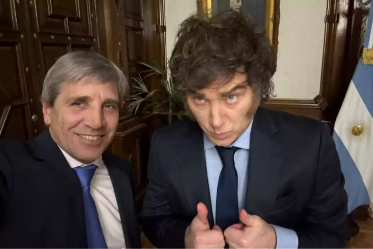 Dos hombres en traje posan para una foto en un entorno formal con una bandera argentina al fondo.