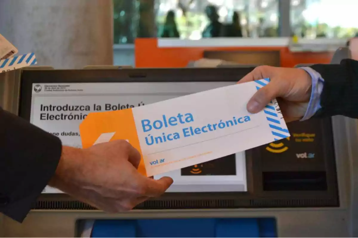 Una persona sostiene una boleta única electrónica frente a una máquina de votación.