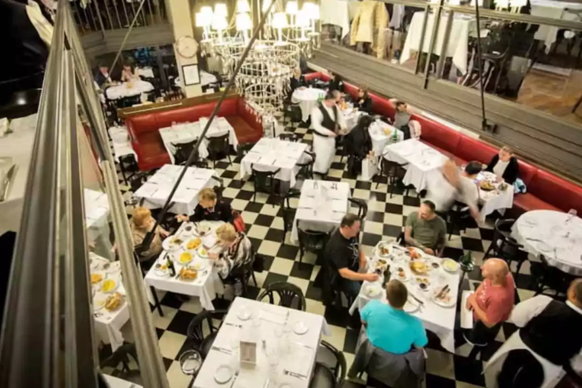 Aerial view of a restaurant with black and white tiled floor, tables with white tablecloths, diners enjoying their meals, and waiters serving. Aerial view of a restaurant with black and white tiled floor, tables with white tablecloths, diners enjoying their meals, and waiters serving.