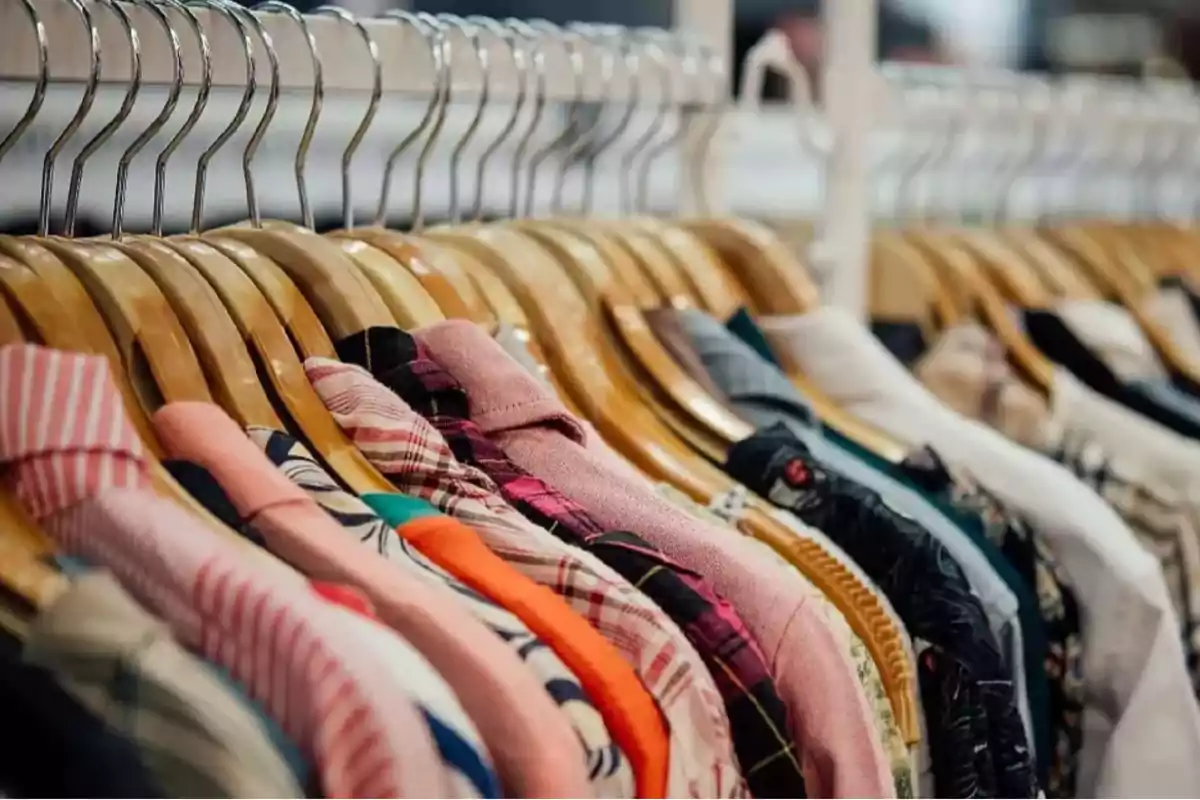 Ropa de varios colores colgada en perchas de madera en una tienda. Ropa de varios colores colgada en perchas de madera en una tienda.