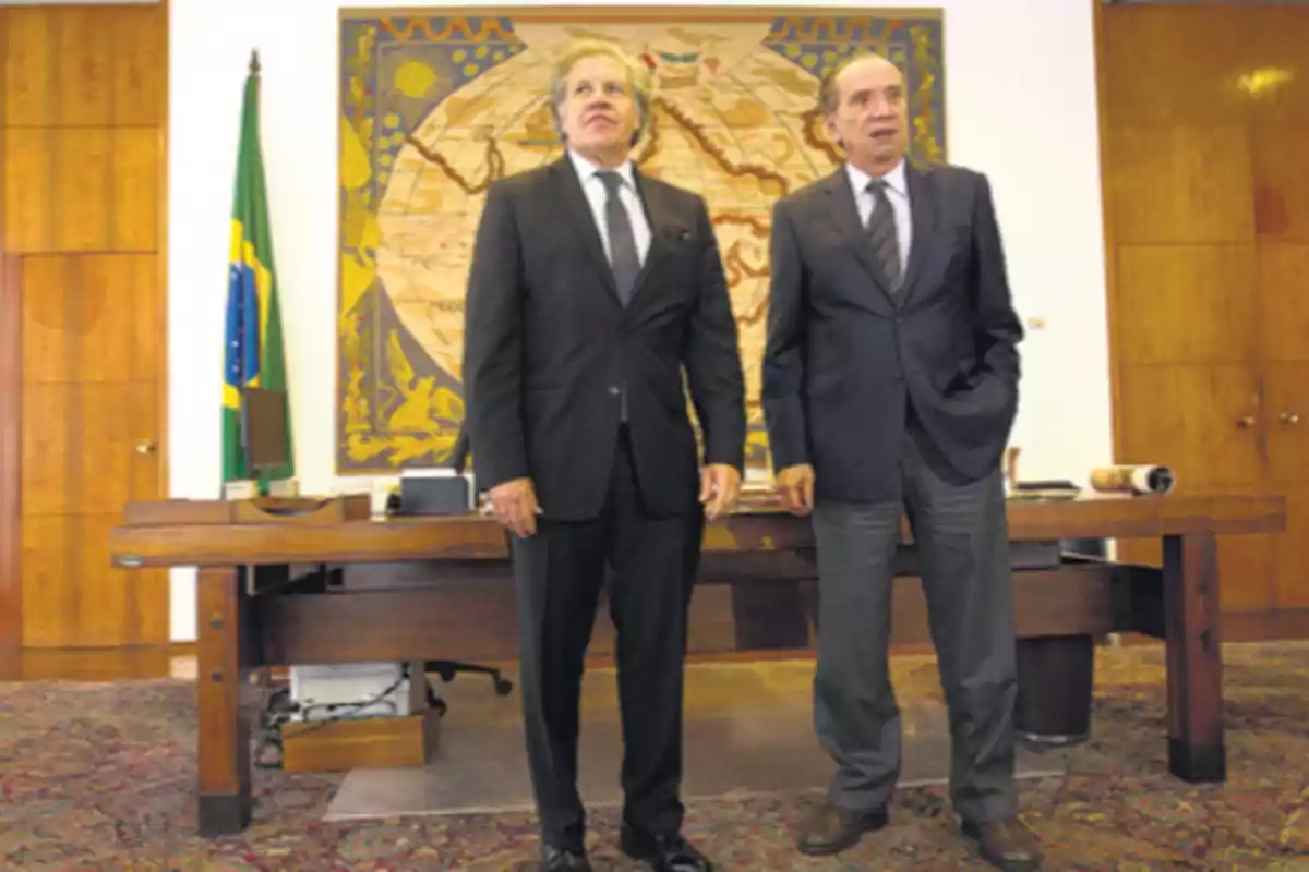 Dos hombres de pie en una oficina con una bandera de Brasil y un mapa grande en la pared detrás de ellos. Dos hombres de pie en una oficina con una bandera de Brasil y un mapa grande en la pared detrás de ellos.