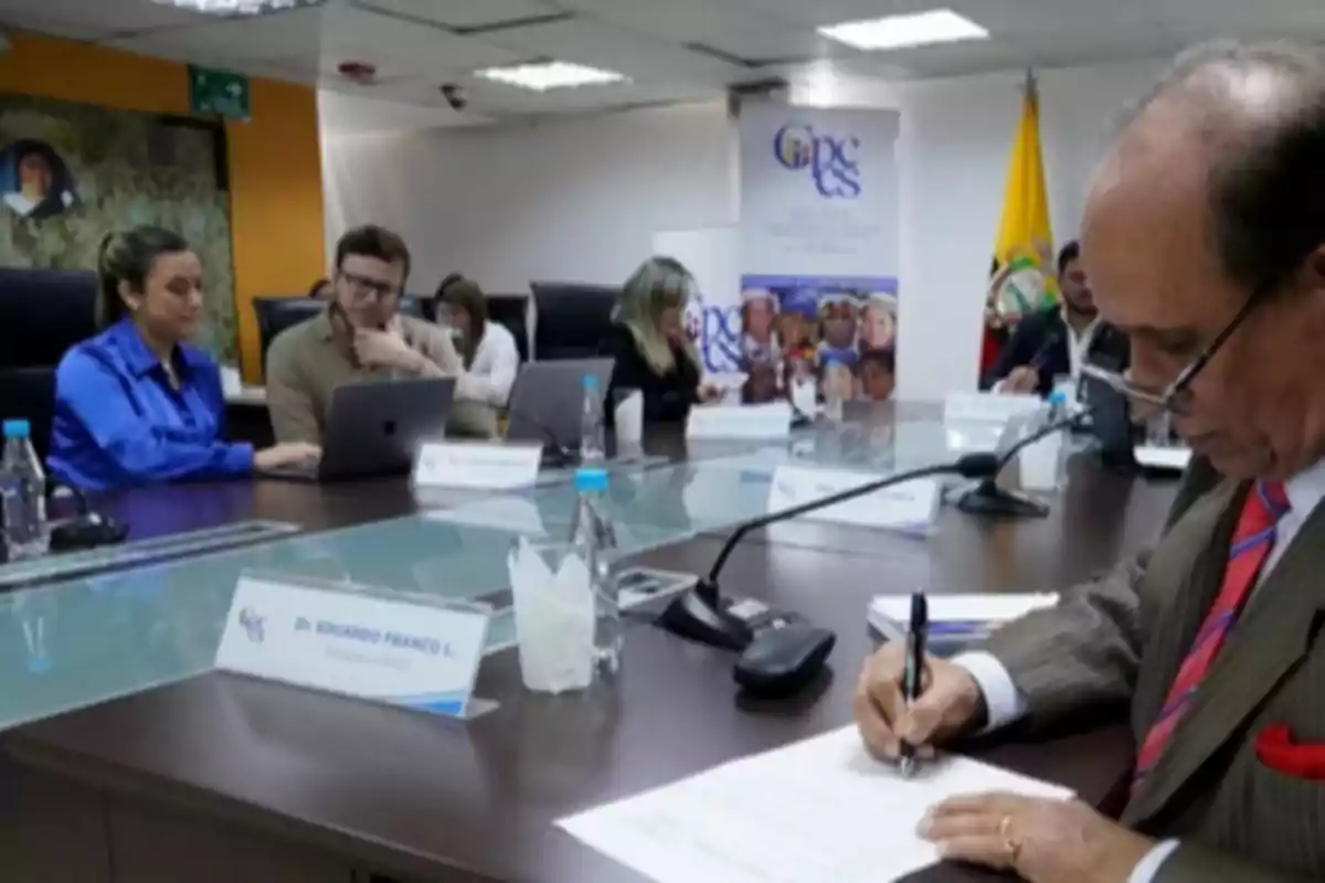 A group of people in a conference room, some working on laptops and others taking notes, with a flag and a poster in the background. A group of people in a conference room, some working on laptops and others taking notes, with a flag and a poster in the background.