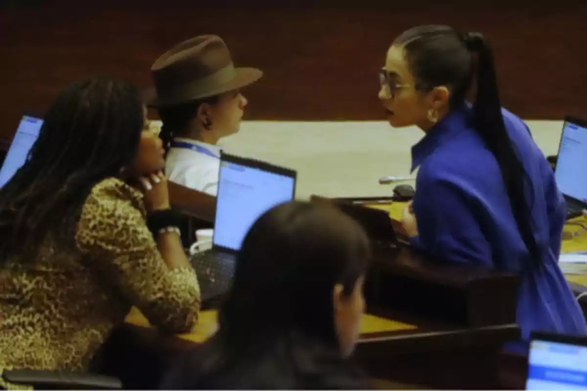 Personas conversando en una sala con computadoras portátiles sobre escritorios. Personas conversando en una sala con computadoras portátiles sobre escritorios.