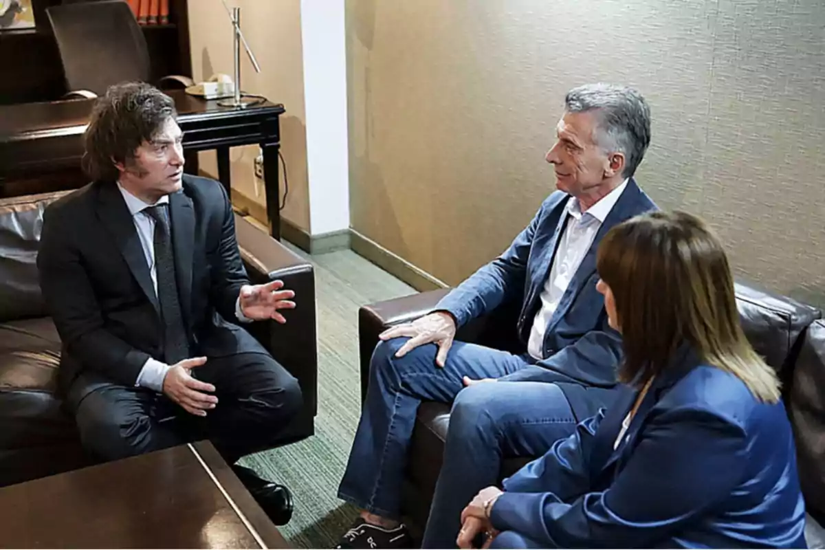 Tres personas sentadas en una sala de reuniones conversando.