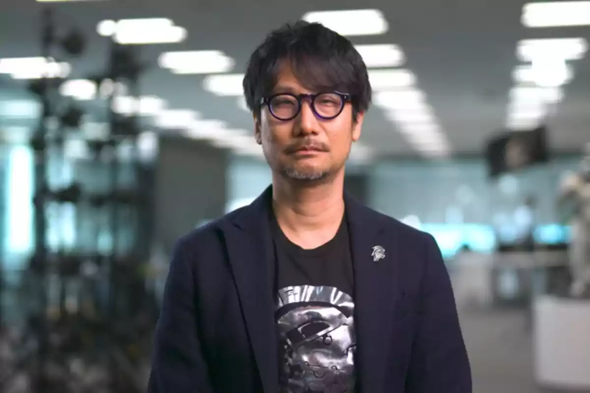 Un hombre con gafas y barba, vestido con una chaqueta oscura y una camiseta con diseño, en un entorno de oficina moderna.