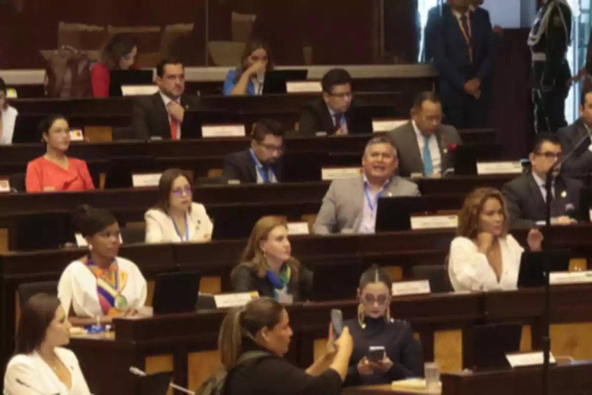 People seated in a legislative chamber with laptops and documents. People seated in a legislative chamber with laptops and documents.