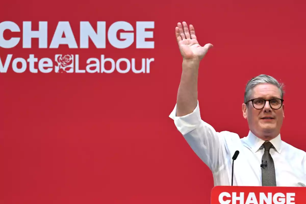 A man with glasses and a tie raises his hand in front of a red background with the text "CHANGE Vote Labour".