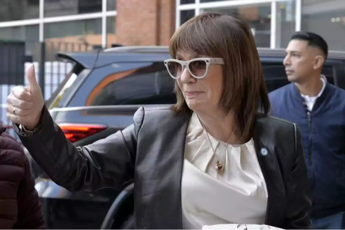 Una persona con gafas de sol y chaqueta de cuero hace un gesto de aprobación con el pulgar hacia arriba mientras camina por la calle. Una persona con gafas de sol y chaqueta de cuero hace un gesto de aprobación con el pulgar hacia arriba mientras camina por la calle.