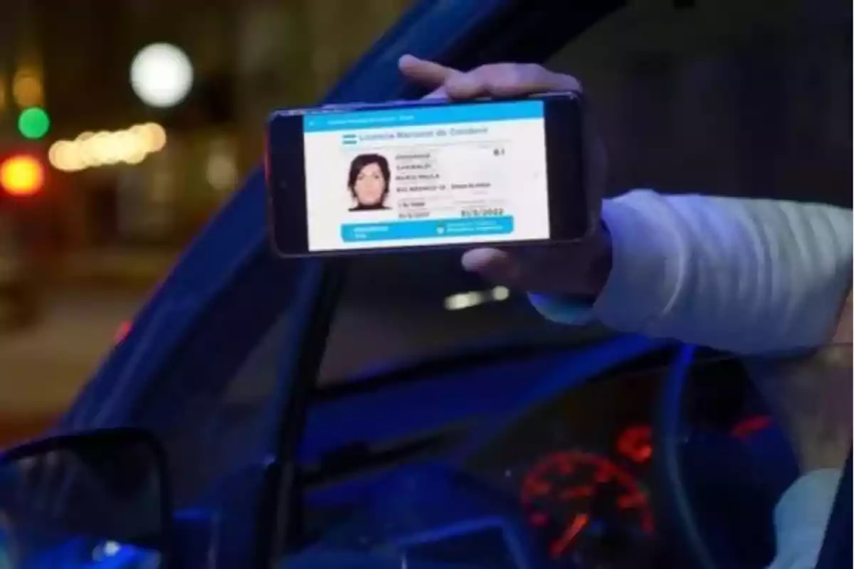 Una persona dentro de un automóvil sostiene un teléfono móvil que muestra una licencia de conducir digital. Una persona dentro de un automóvil sostiene un teléfono móvil que muestra una licencia de conducir digital.