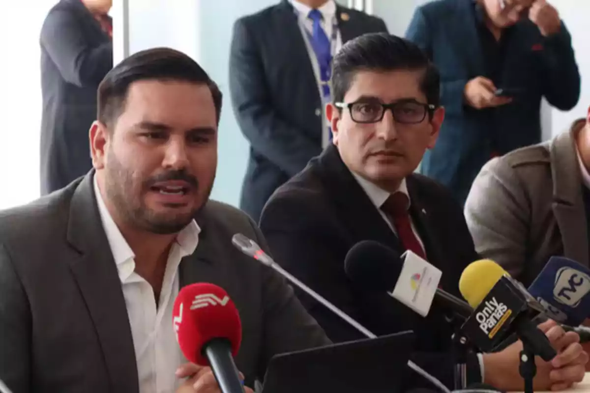 Dos hombres en una conferencia de prensa con varios micrófonos frente a ellos. Dos hombres en una conferencia de prensa con varios micrófonos frente a ellos.