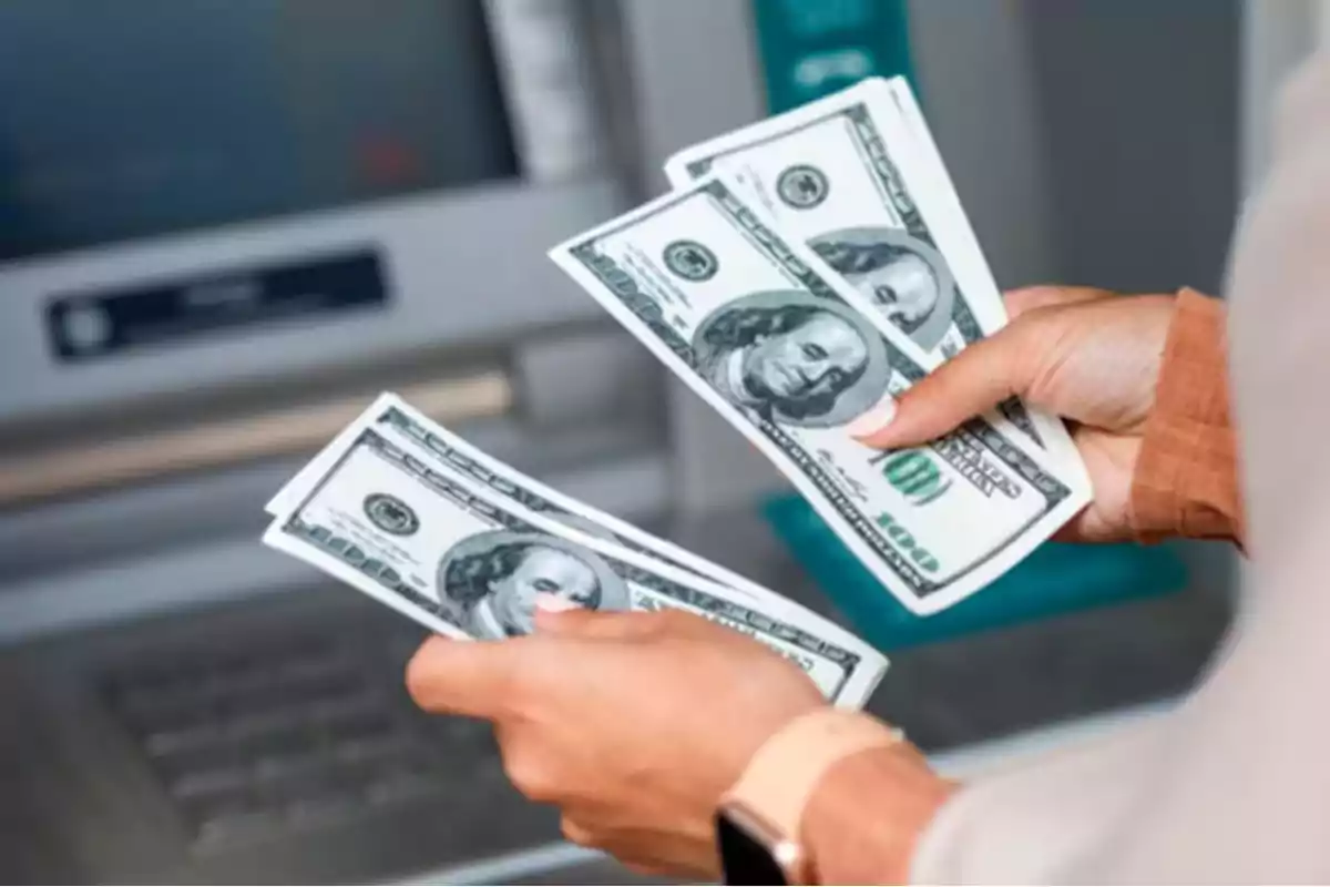 Person counting hundred-dollar bills in front of an ATM.
