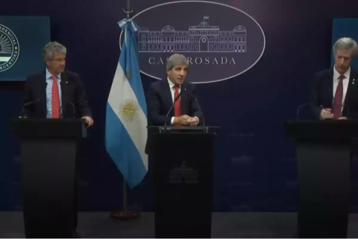 Tres personas en un podio durante una conferencia de prensa en la Casa Rosada con la bandera de Argentina al fondo.
